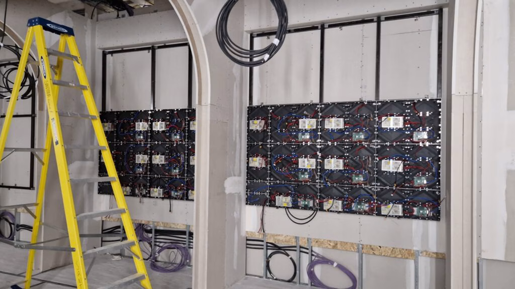 Teilweise montierte LED-Module an der Wand einer Baustelle, davor eine Leiter und offen liegende Kabel